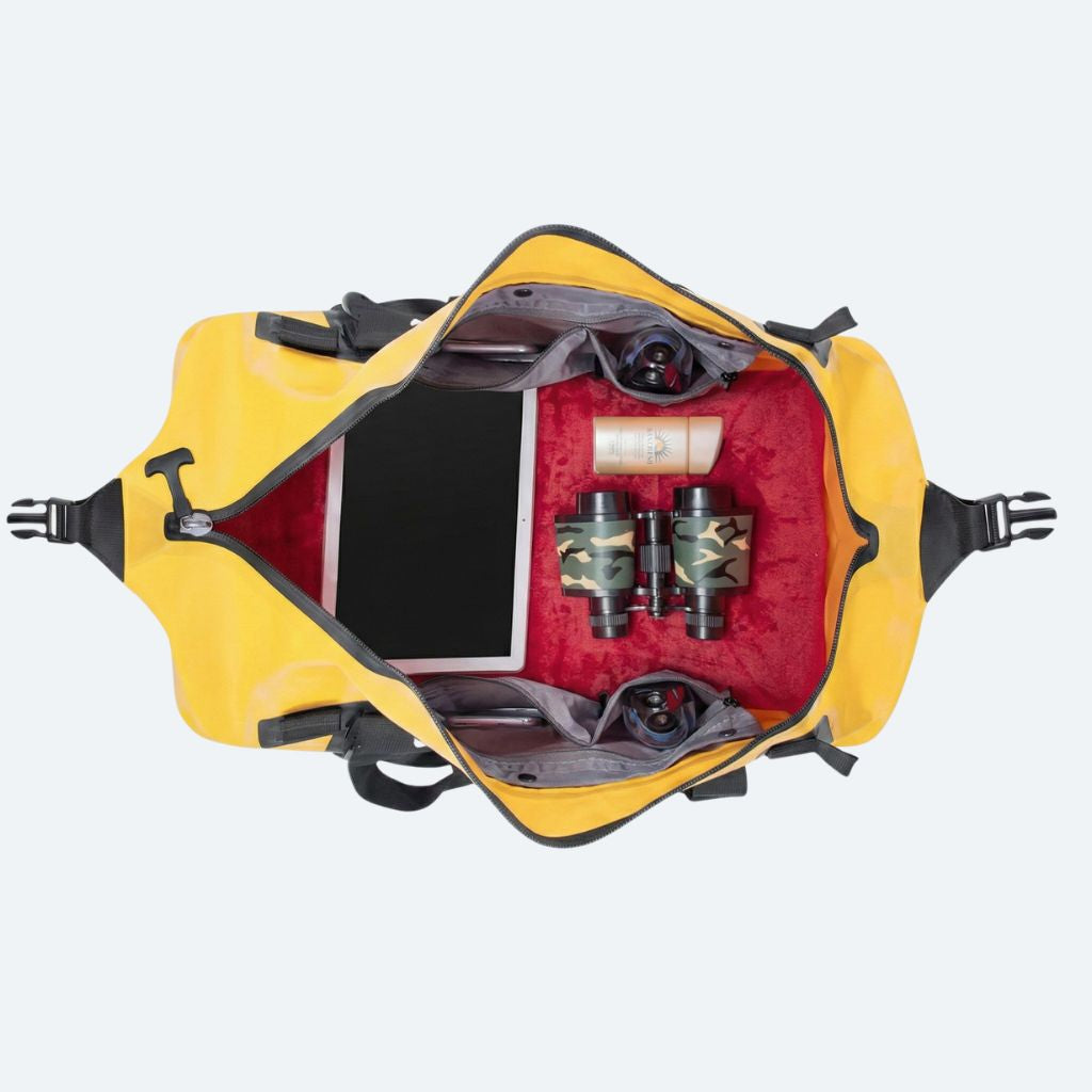 Sac de voyage étanche jaune 50L ouvert de dessus, intérieur rouge avec tablette, jumelles et accessoires rangés