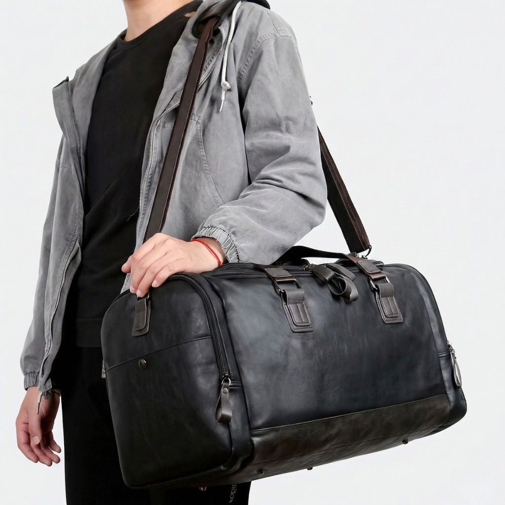 Homme portant un Duffle Bag cabine noir en simili cuir grainé en bandoulière sur l'épaule