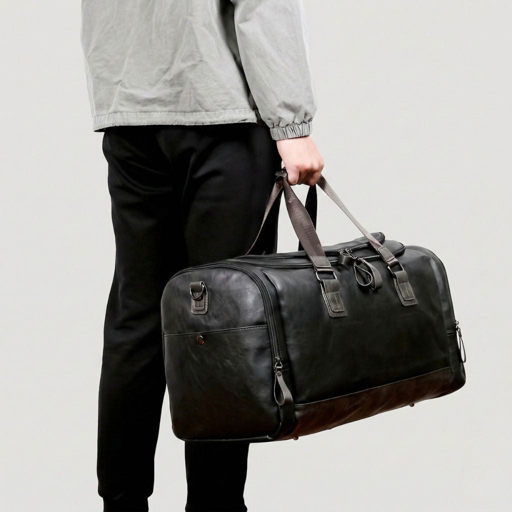 Port main du Duffle Bag cabine noir, homme tenant les poignées marron, format cylindrique en simili cuir