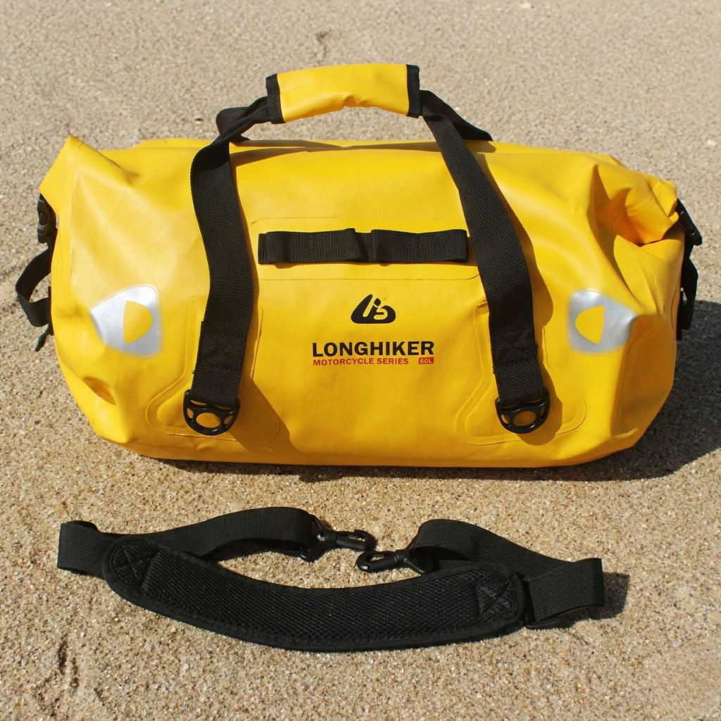 Sac de voyage étanche jaune 40L format duffle compact posé sur sable avec bandoulière noire réglable détachée