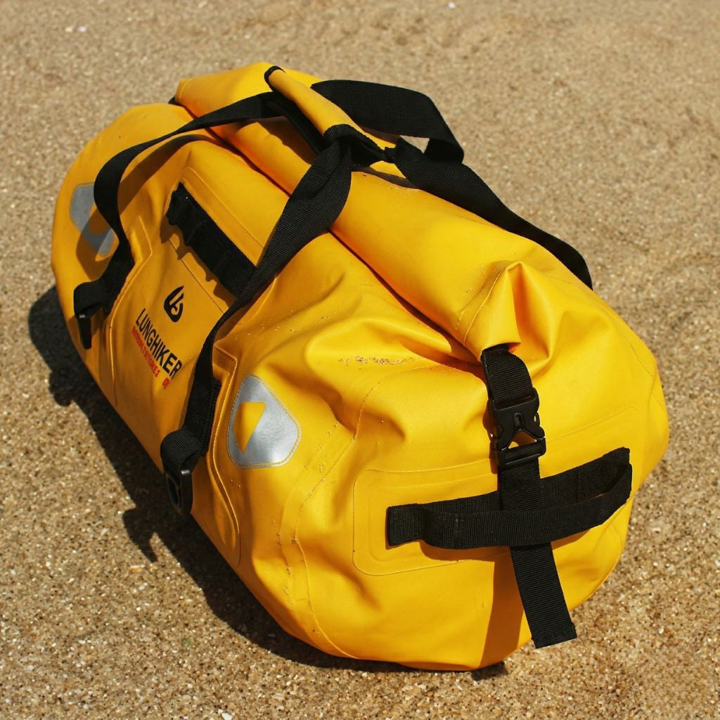 Sac de voyage étanche jaune format duffle cylindrique vu de côté posé sur sable, silhouette compacte et robuste Image