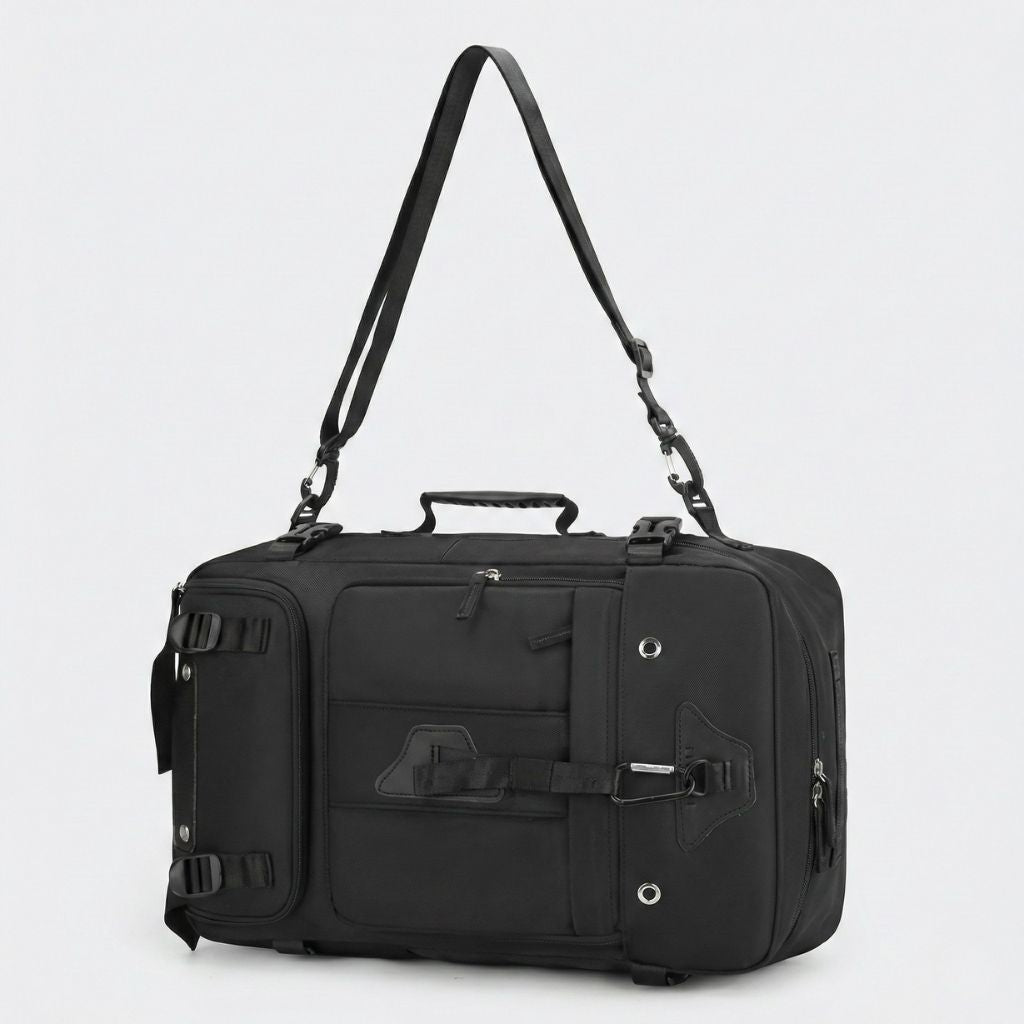 Sac de voyage noir porté à la main par sa bandoulière longue, en mode duffle, poignée de transport en haut