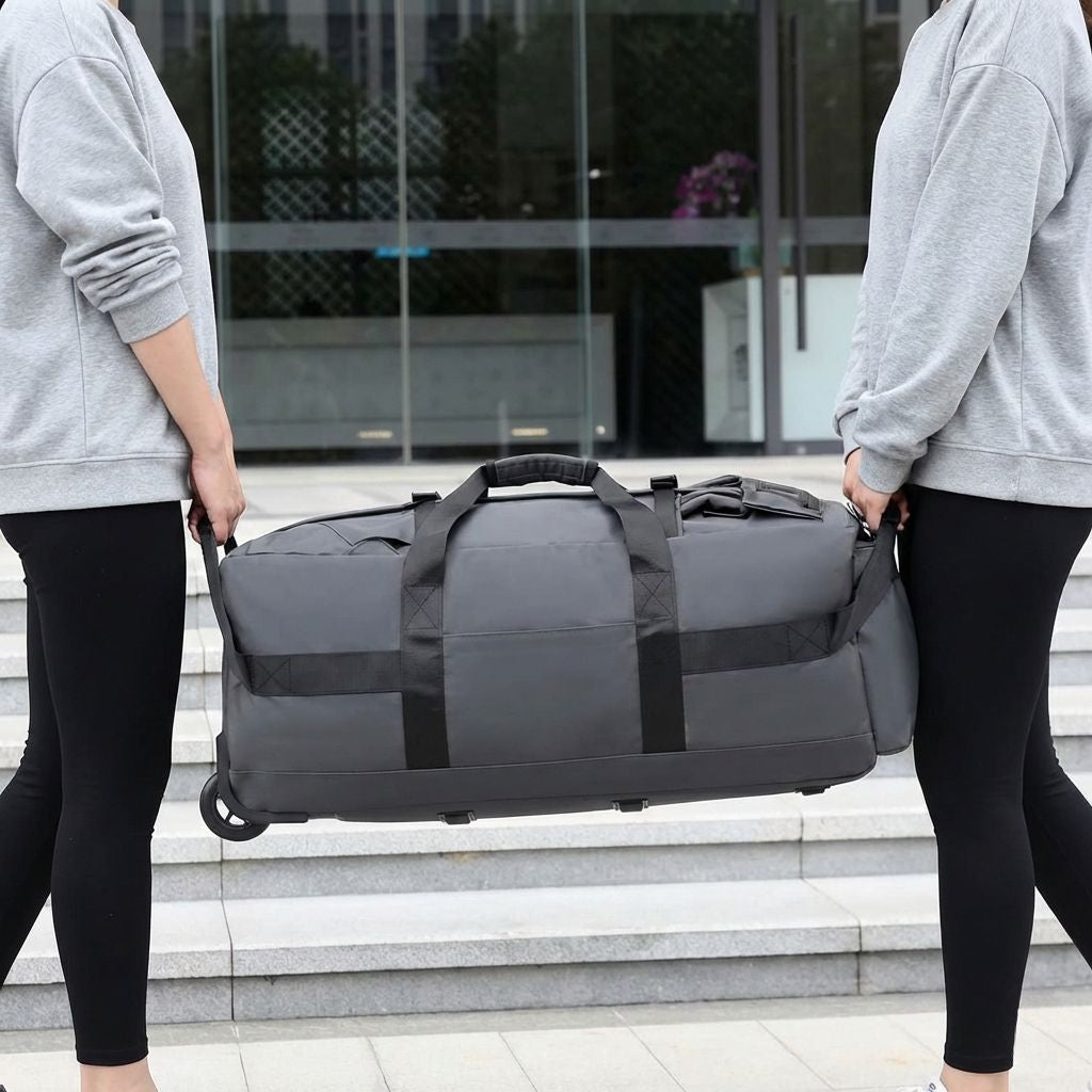 Deux personnes portant ensemble un grand sac de voyage gris par ses poignées latérales devant un bâtiment urbain Image