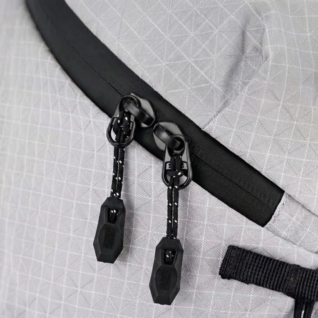 Gros plan sur les doubles curseurs noirs en cordelette du sac à dos randonnée léger en tissu ripstop gris clair.