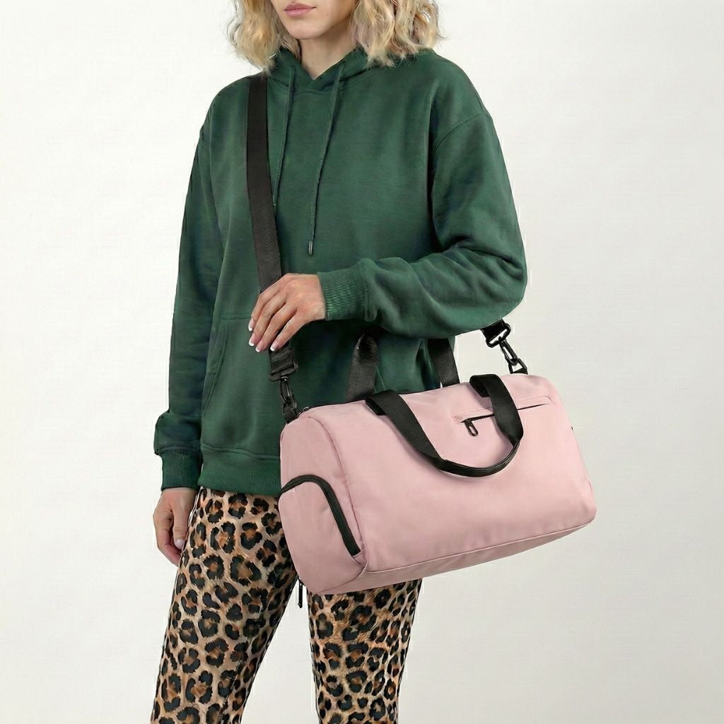 Petit sac de voyage imperméable rose avec bandoulière réglable et poignées noires, porté à l’épaule Image