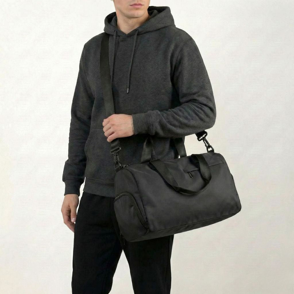 Homme en sweat gris portant sur l'épaule un sac de sport voyage noir compact avec bandoulière réglable Image