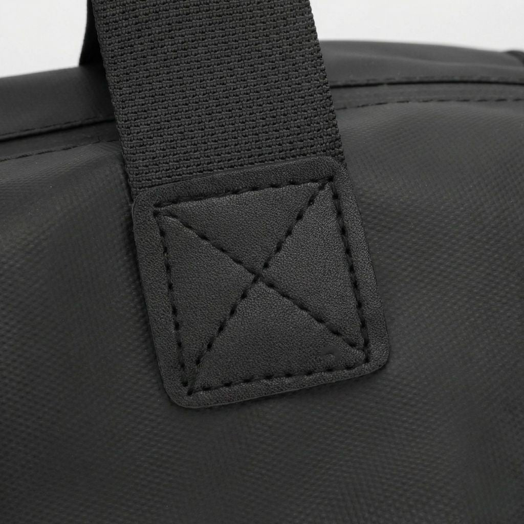 Gros plan de l'attache anse du sac de voyage sport homme noir, couture renforcée en croix sur cuir