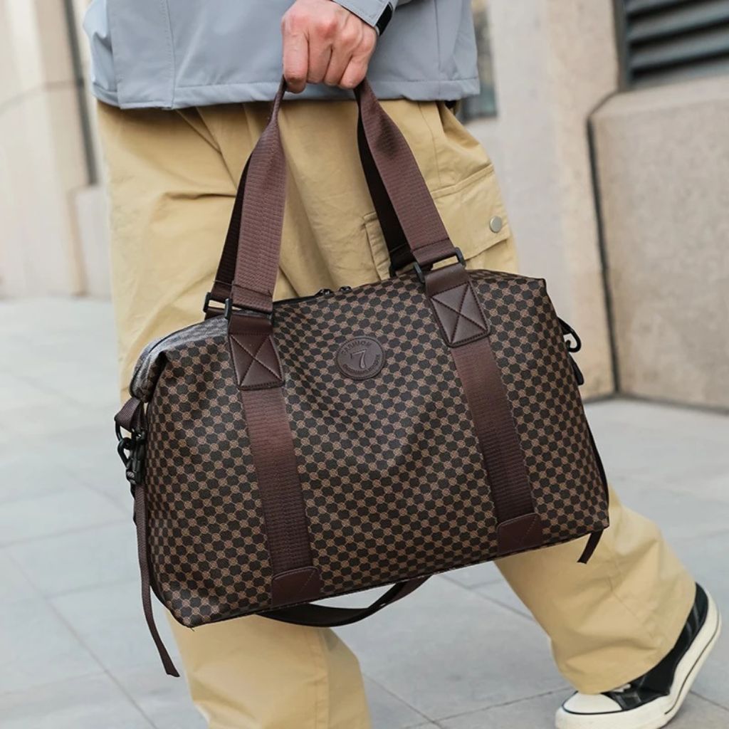 Homme tenant un sac de voyage à motif damier brun par ses poignées, milieu urbain extérieur ensoleillé Image