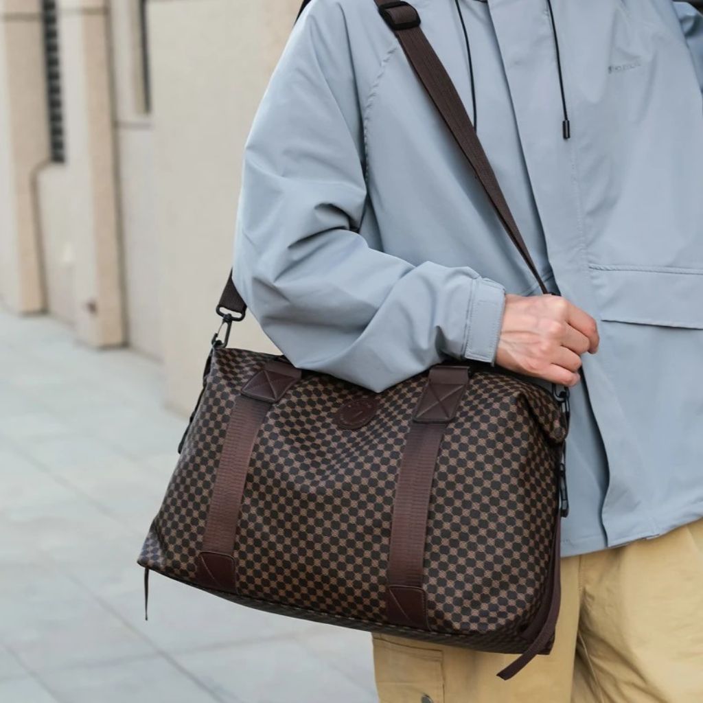 Homme portant en bandoulière un sac de voyage à motif damier brun et beige, style urbain décontracté Image