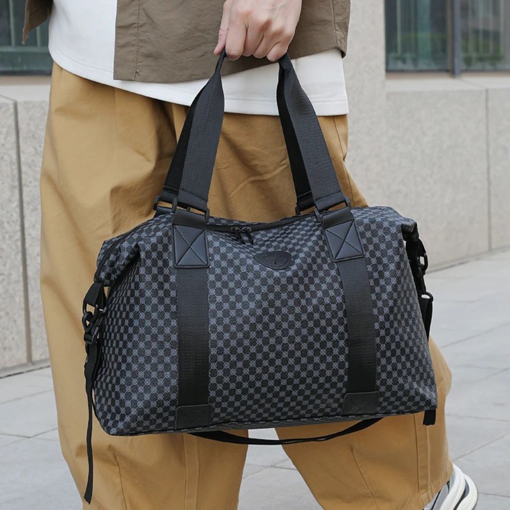 Homme tenant à deux mains un sac de voyage à motif damier noir et anthracite, format cabine week-end Image