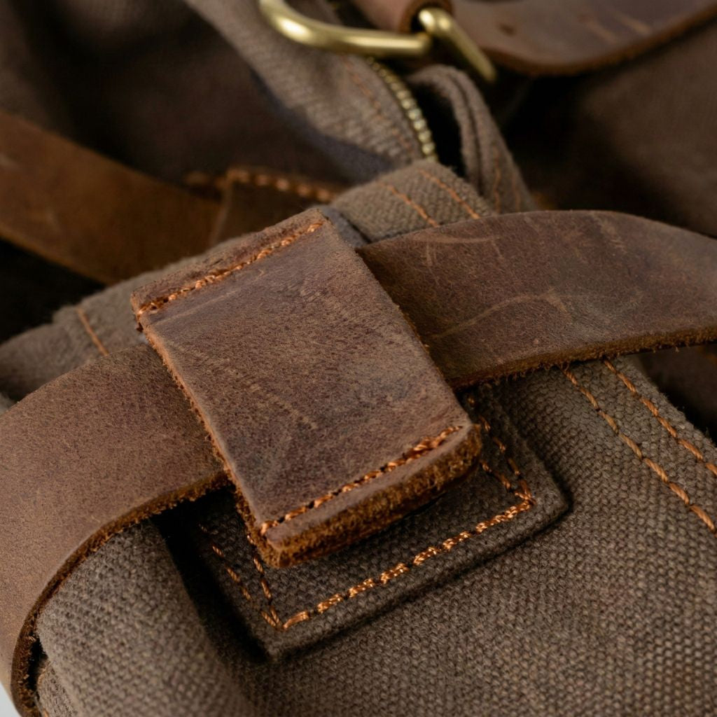 Gros plan de la lanière cuir brut et de la boucle en laiton sur le canvas waxé du sac besace XL
