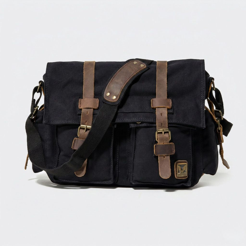 Face avant du sac besace XL noir avec large lanière cuir marron contrastante, quatre poches et boucles laiton
