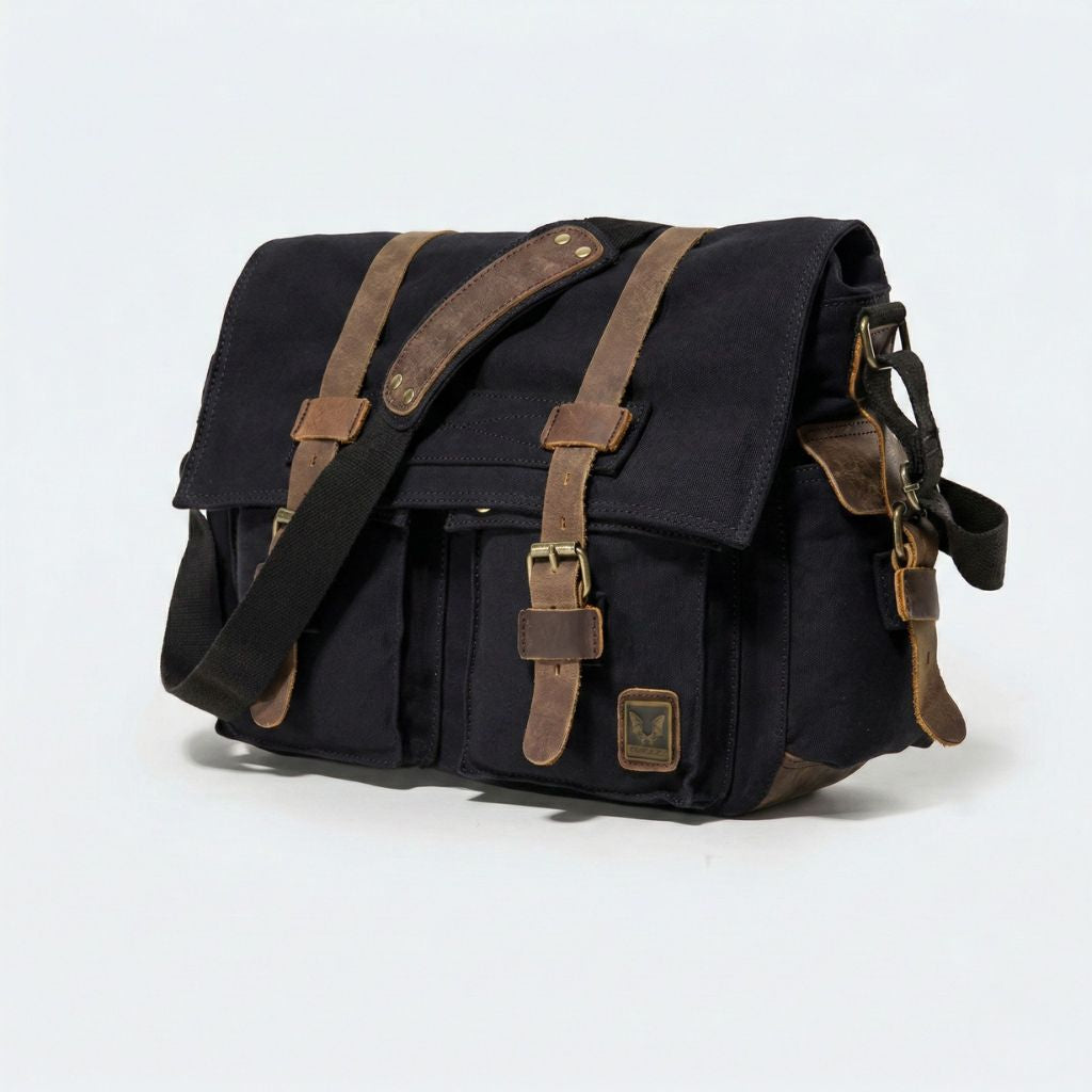 Sac besace XL noir vue 3/4 : canvas noir, renforts cuir marron contrastants et quatre poches à boucles laiton