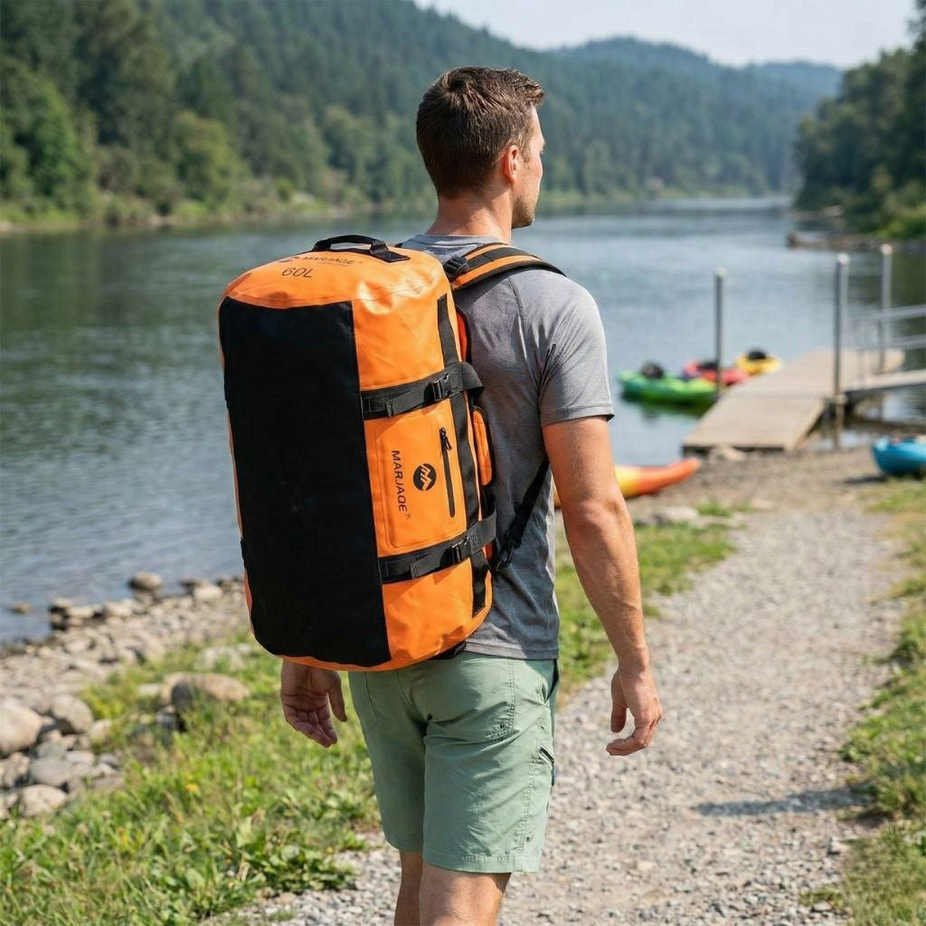 Homme de dos portant un sac de voyage étanche orange en mode sac à dos au bord d'un lac, kayaks en arrière-plan Image