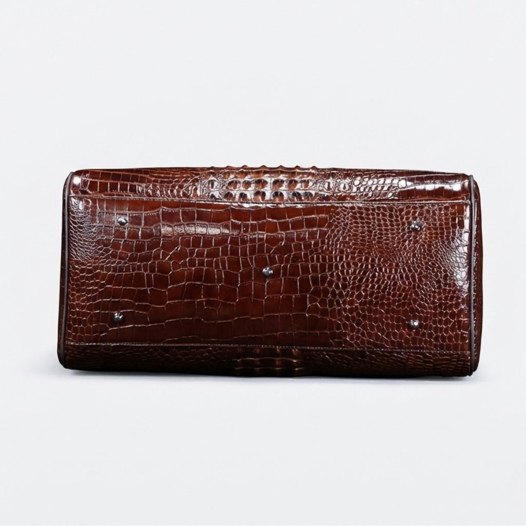 Dessous du sac de voyage cuir croco marron, quatre pieds protecteurs argentés et coutures de renfort