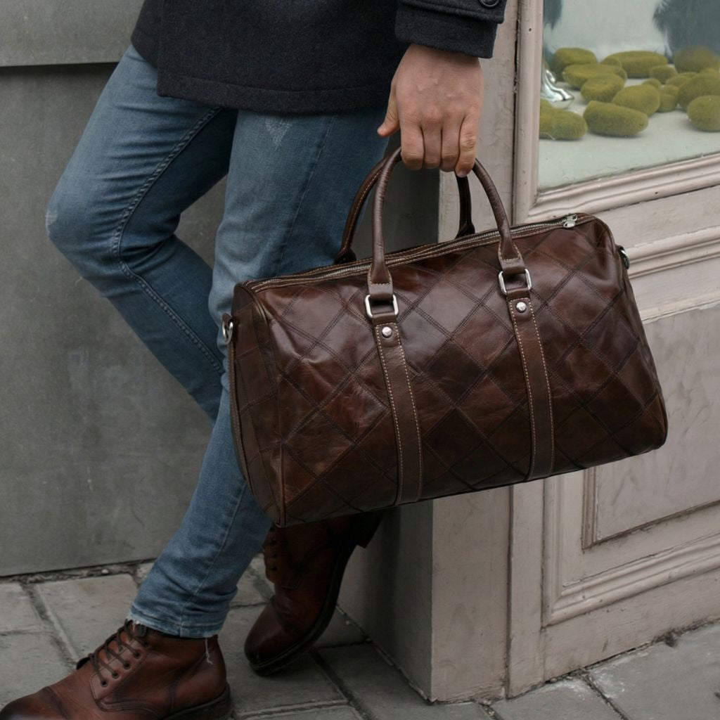 Homme tenant à la main un sac de voyage en cuir brun foncé motif matelassé, devant une devanture de magasin Image