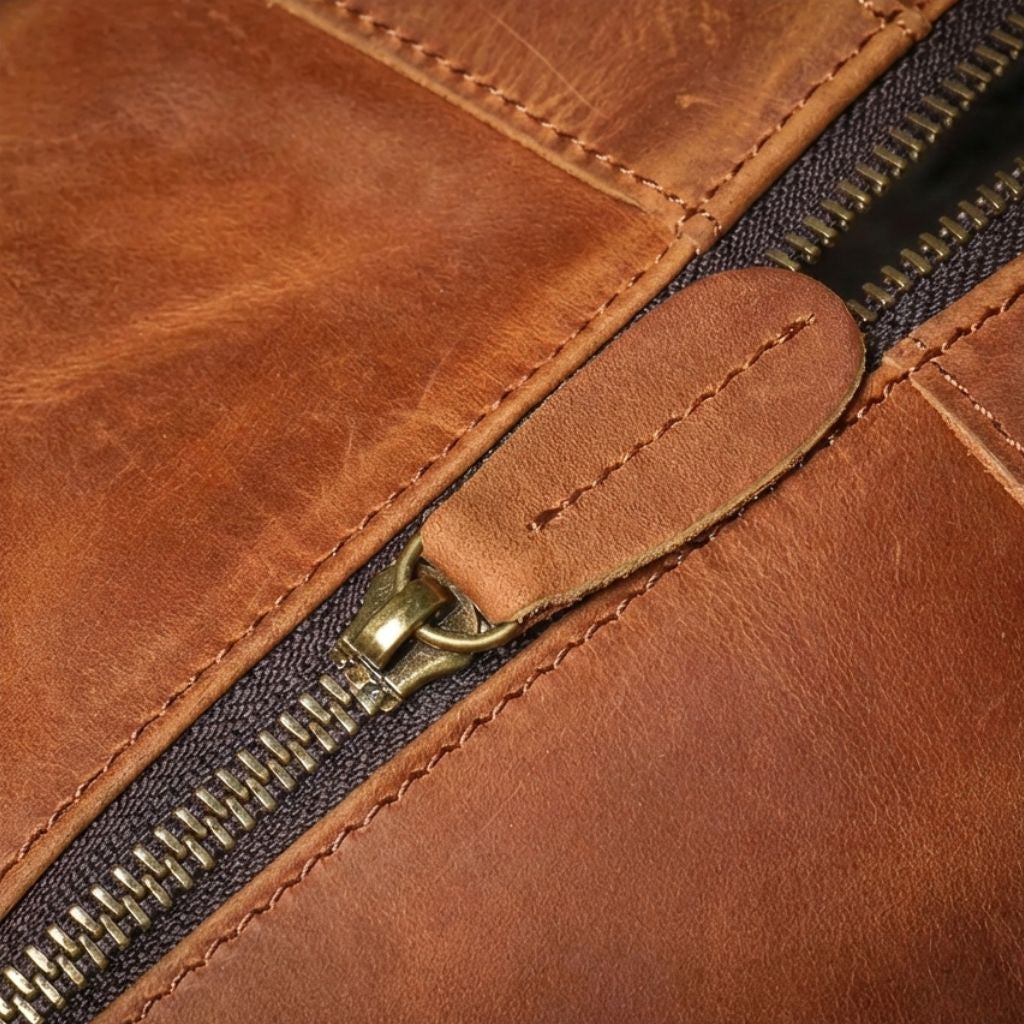 Gros plan sur la fermeture éclair laiton de la poche avant avec tirette en cuir cognac et couture en croix