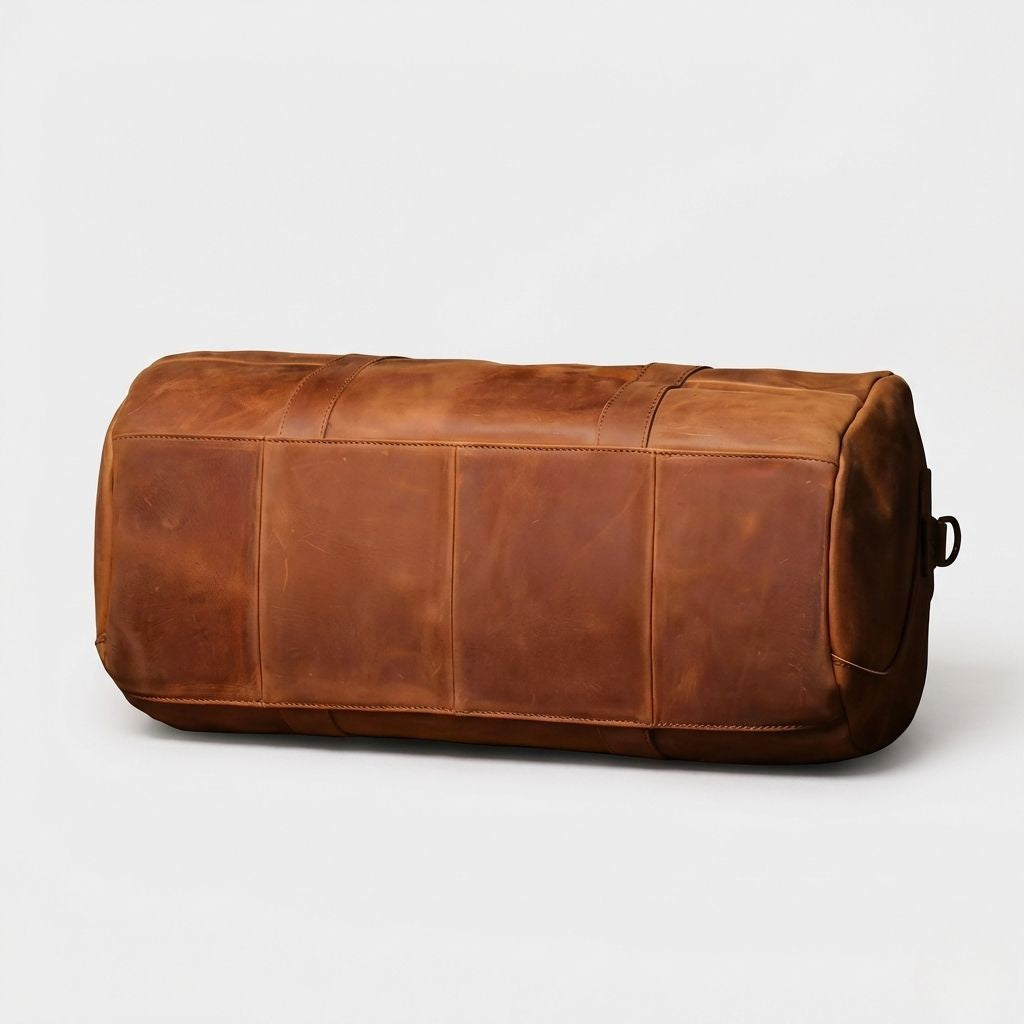 Dessous du sac de voyage cuir cognac vintage, assemblage en panneaux cousus et patine naturelle du cuir
