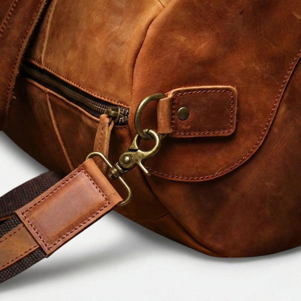 Gros plan de l'anneau de fixation bandoulière et du mousqueton en laiton d'un sac de voyage en cuir cognac Image