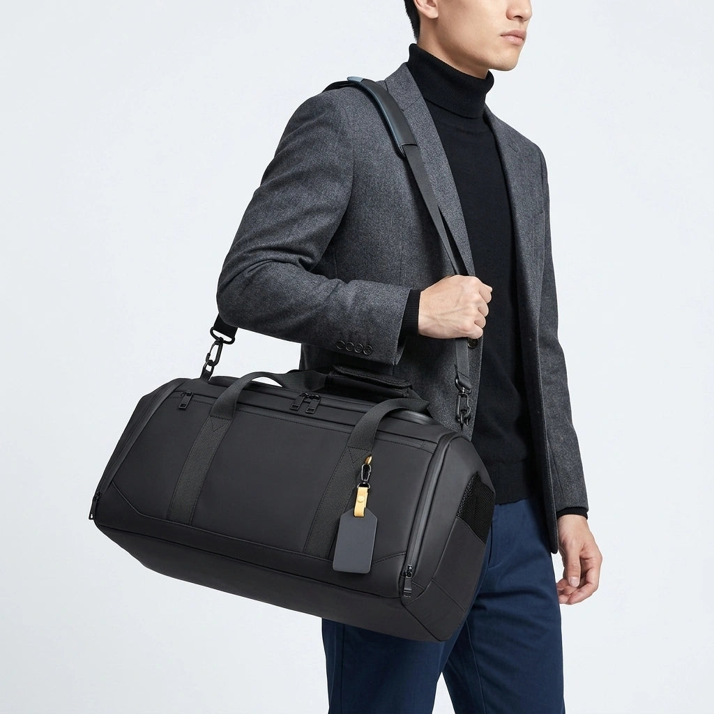 Homme en veste gris portant un sac week-end noir 25L en bandoulière avec étiquette de bagage dorée