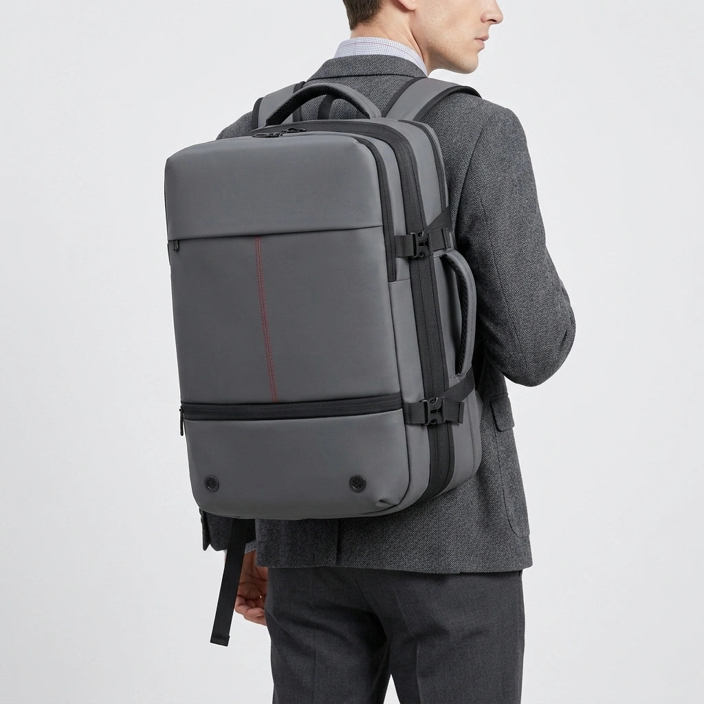 Homme en costume gris portant un sac à dos de voyage business extensible coloris gris avec liseré rouge