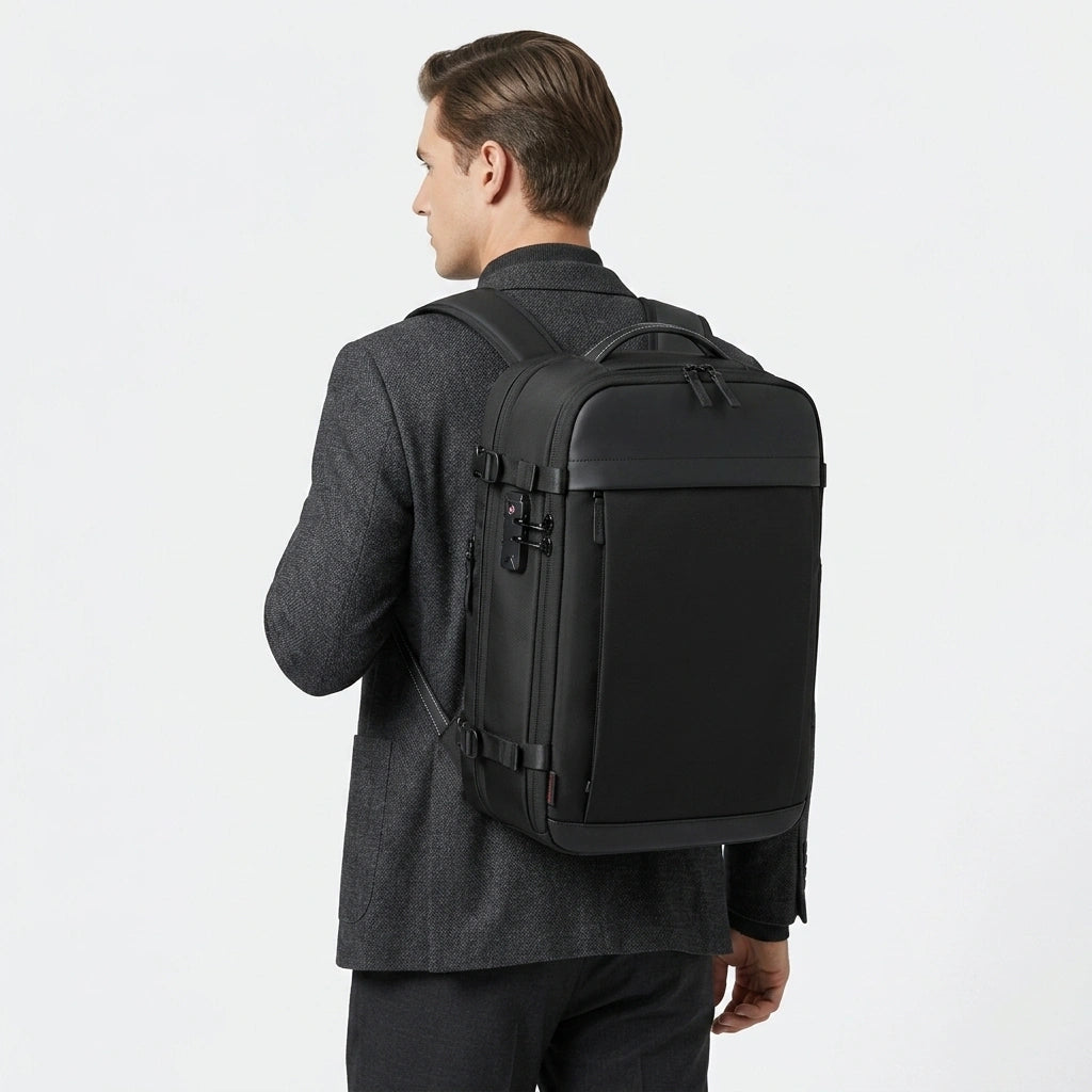 Homme en blazer gris portant le sac à dos cabine noir vu de dos avec cadenas TSA visible sur le côté