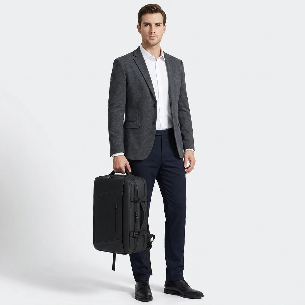 Homme en blazer gris et chemise blanche tenant le sac à dos cabine noir par la poignée, vue en pied