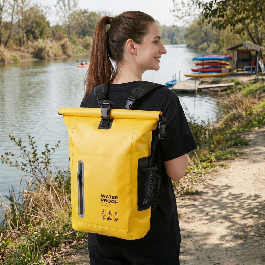 Femme portant un sac à dos étanche roll-top jaune au bord d'une rivière avec des kayaks colorés en arrière-plan Image