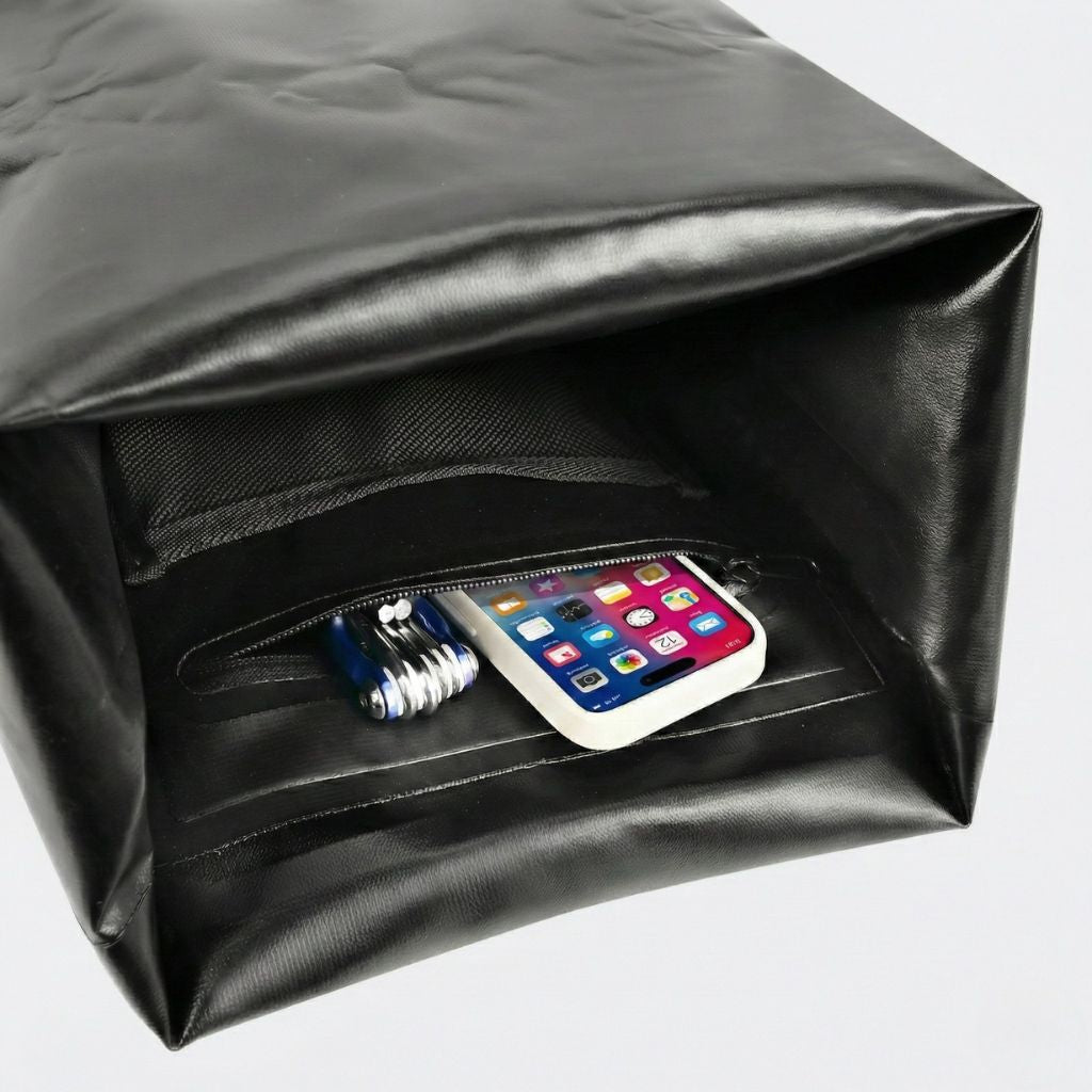 Compartiment roll-top ouvert d'un sac à dos étanche noir révélant un smartphone et des accessoires connectiques Image