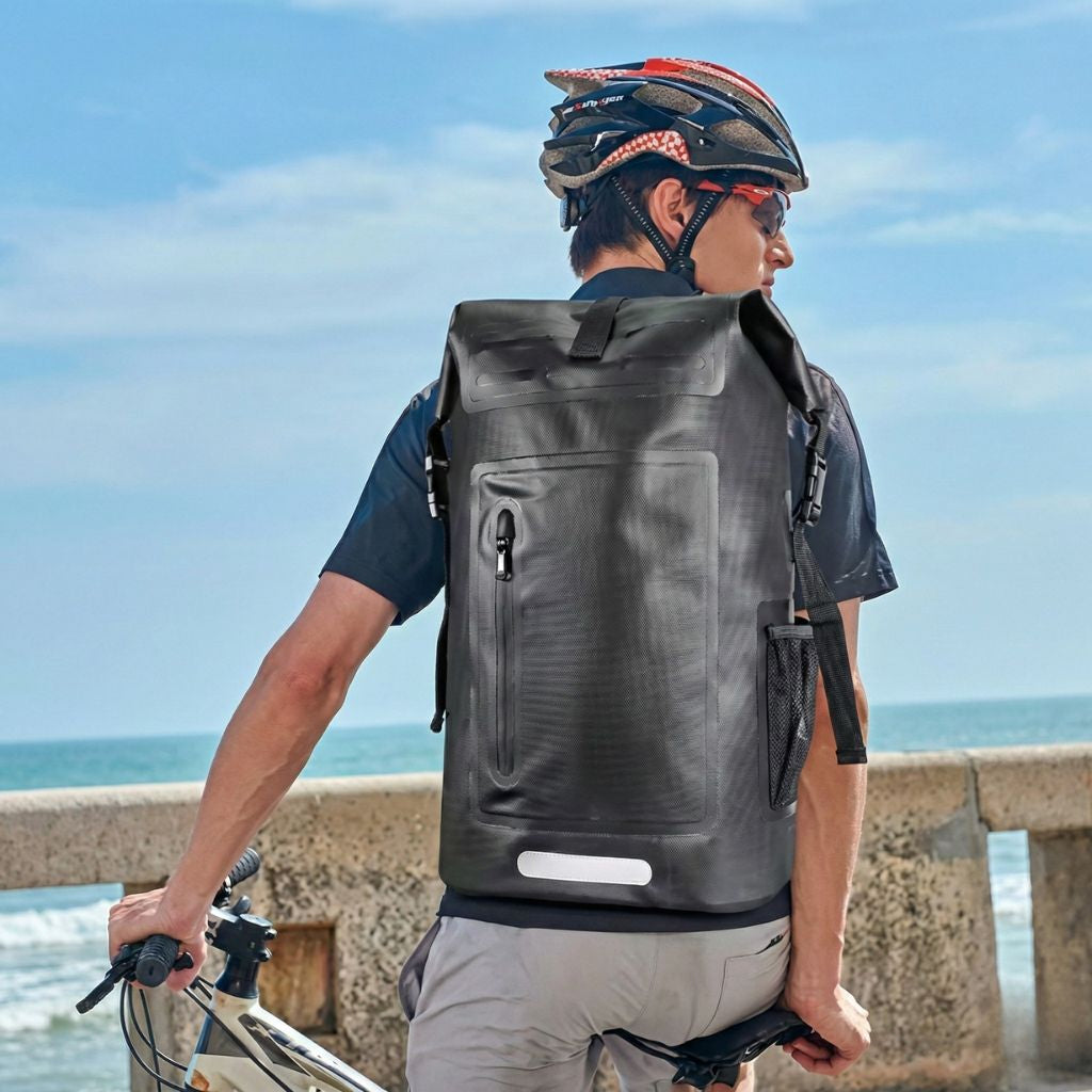 Cycliste au bord de la mer portant le sac à dos étanche noir roll-top 28L sur son vélo de route