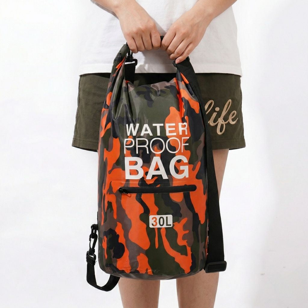 Femme tenant devant elle un sac étanche camouflage orange et kaki 30L, vue de face, poche zippée visible