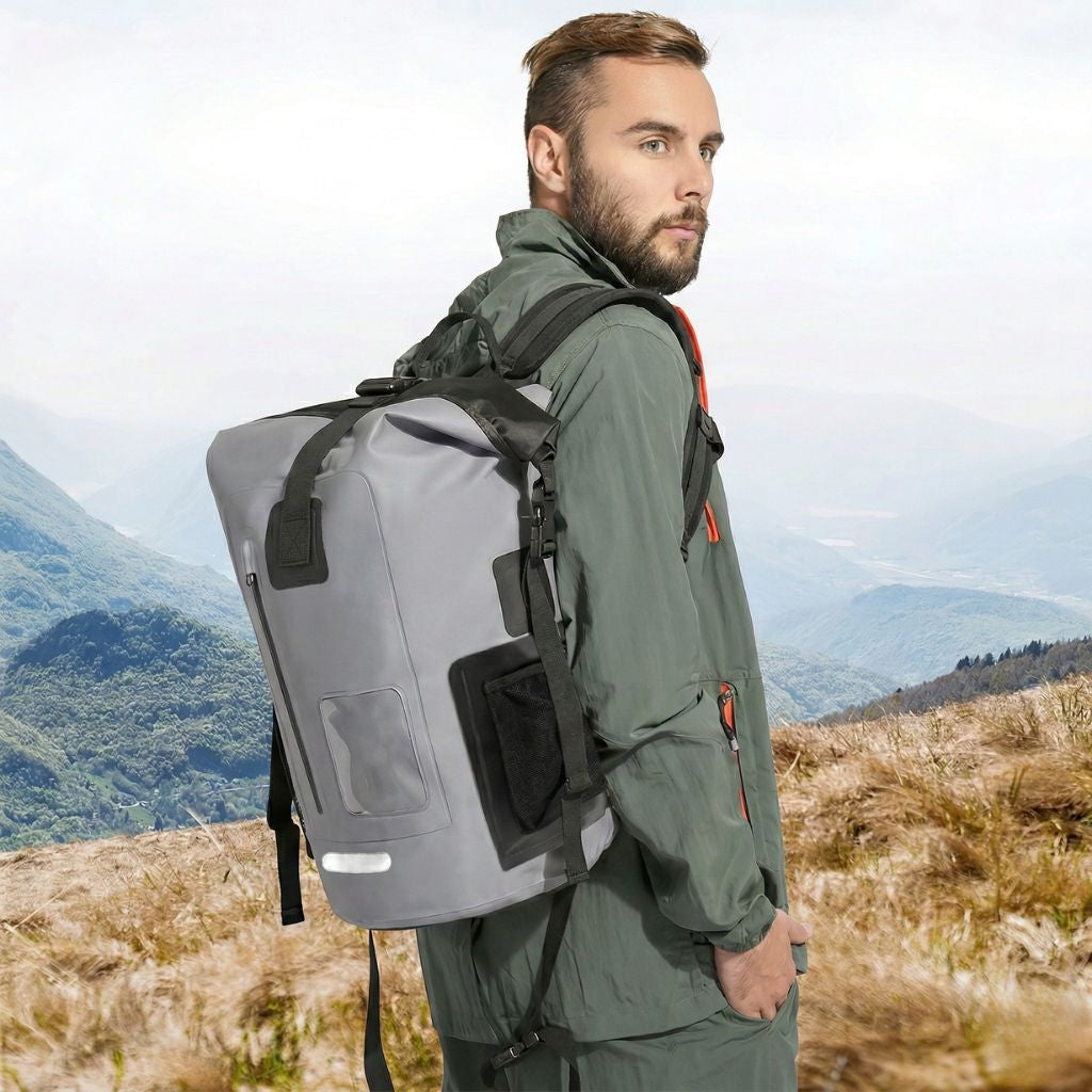Homme portant un sac à dos étanche gris 30L en montagne, vue de profil, bretelles larges et fermeture roll-top