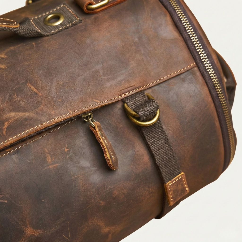 Poche latérale zippée sur cuir brun patiné, tirette cuir cognac et sangle canvas avec anneau en D