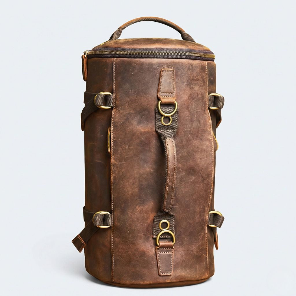Sac cylindrique en cuir brun en position verticale, deux anneaux en D supérieurs et poignée centrale cuir