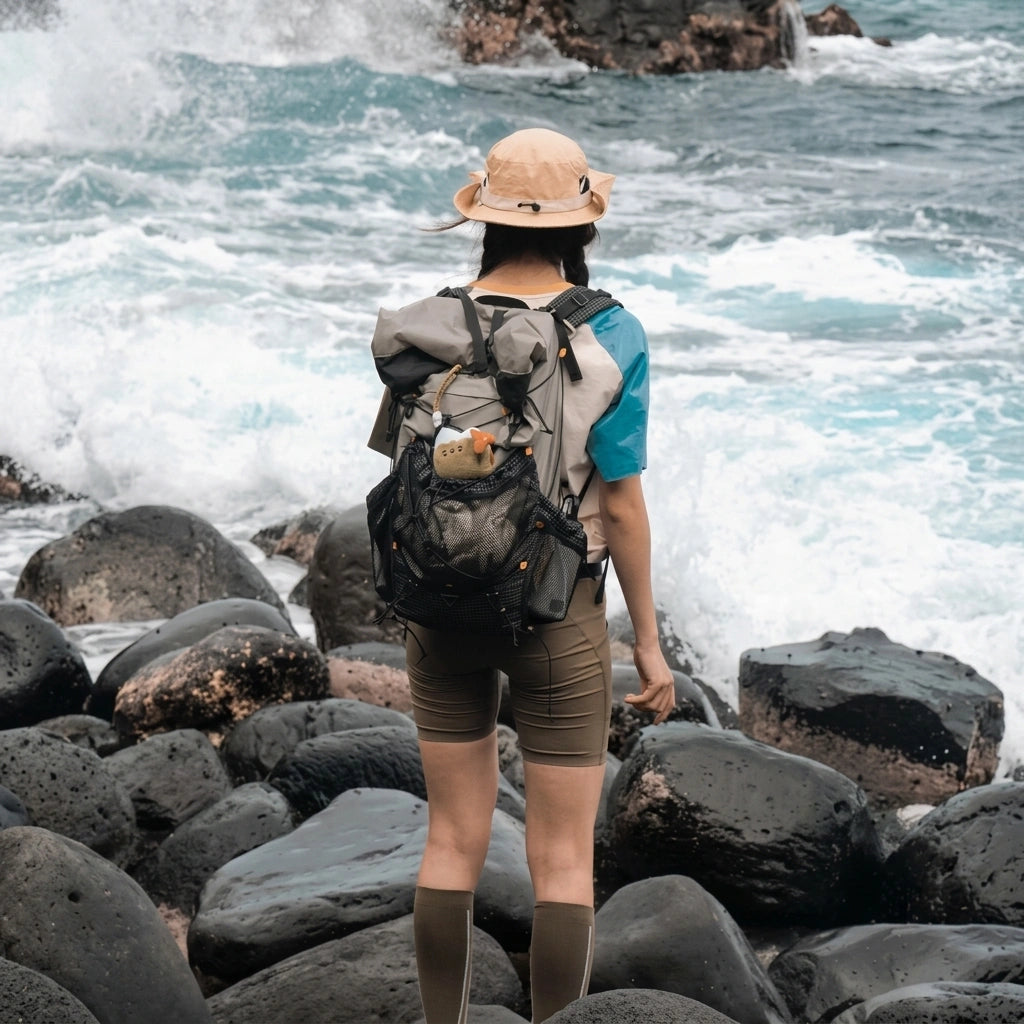 Randonneuse de dos sur des rochers volcaniques portant un sac à dos de trekking gris avec poche filet bien remplie