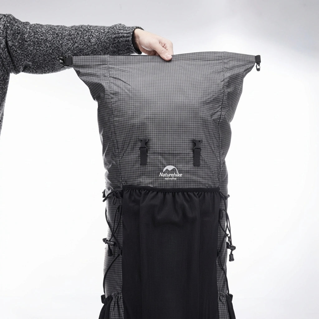 Main tenant par la poignée un sac à dos de randonnée gris foncé avec fermeture rouleau et poche filet noire Image