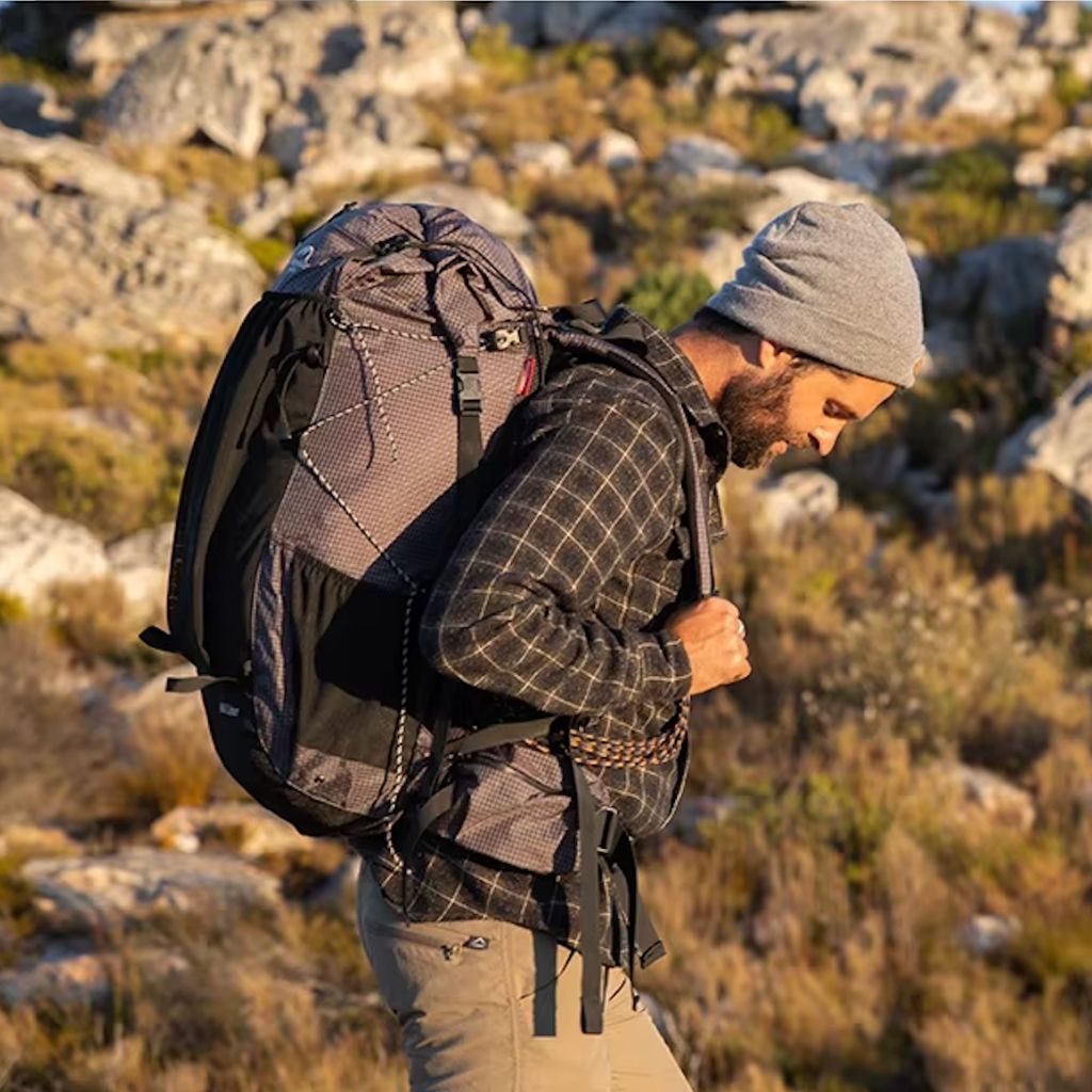Homme de profil en montagne rocheuse réglant les bretelles de son sac à dos de trekking gris 60L