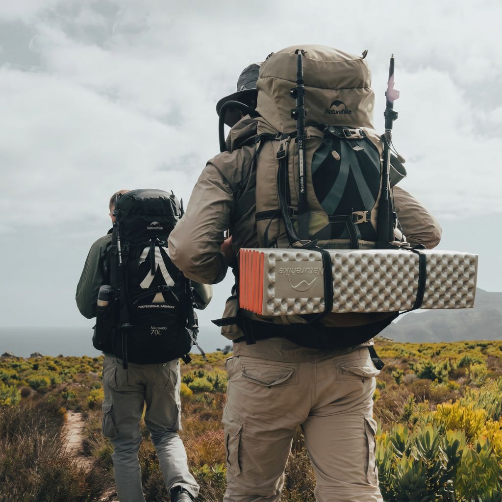 Deux randonneurs de dos sur sentier montagneux portant chacun un grand sac à dos trekking 70L kaki et noir