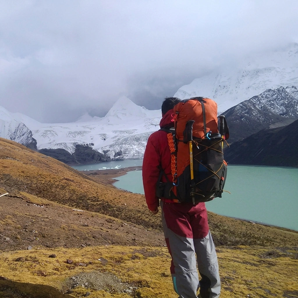 Randonneur de dos avec sac à dos trekking orange 52L devant un lac glaciaire turquoise et des sommets enneigés Image