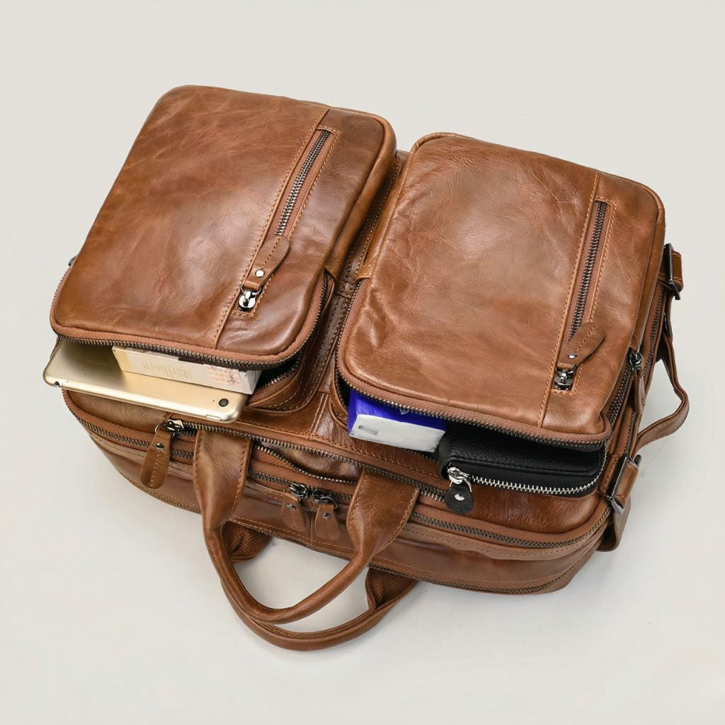 Deux poches avant ouvertes révélant une tablette, un livre et des accessoires électroniques, cuir cognac