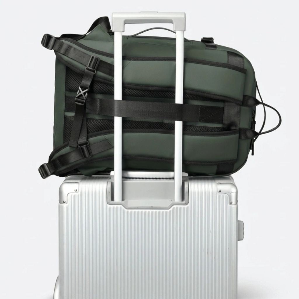 Sac à dos voyage vert fixé sur la poignée télescopique d'une valise grâce à la sangle de passage