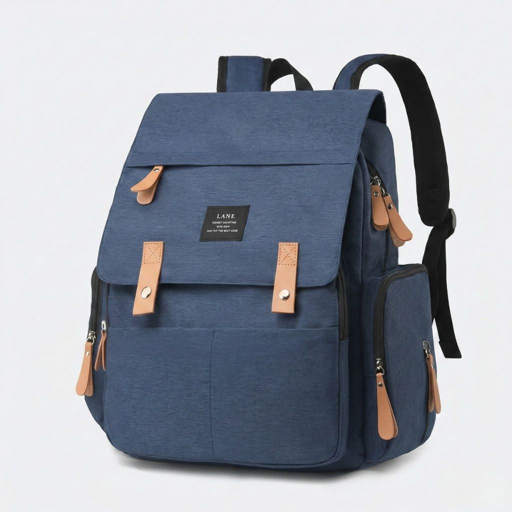 Sac à dos à langer bleu marine uni, vue 3/4 avant, rabat supérieur, attaches cuir camel et poches latérales