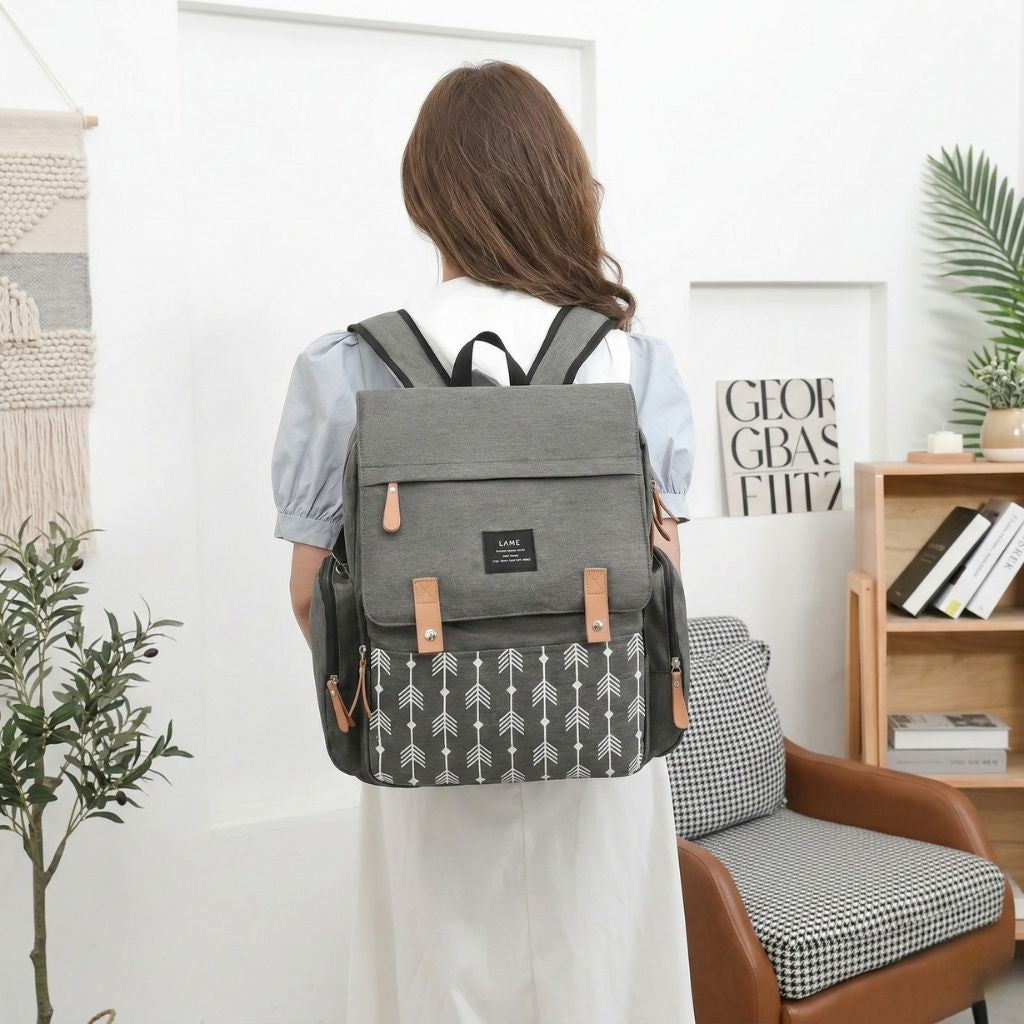 Femme portant le sac à dos à langer gris foncé motif flèches, de dos dans un intérieur moderne et lumineux