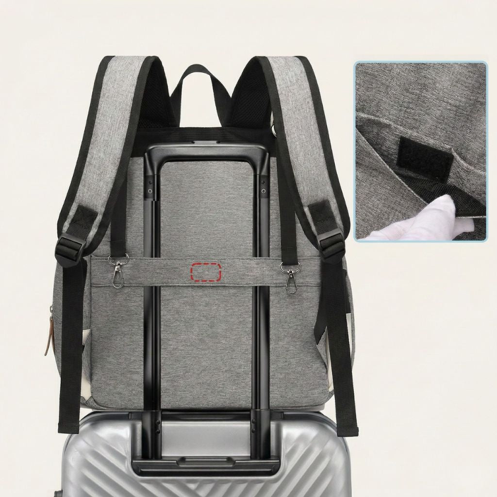 Sac à langer gris fixé sur la poignée télescopique d'une valise à roulettes grâce aux attaches poussette intégrées