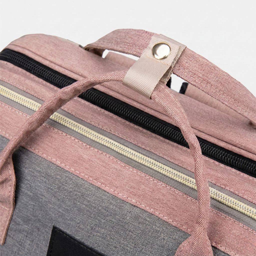 Gros plan des poignées de portage et du zip double tirettes dorées sur le dessus du sac à langer rose