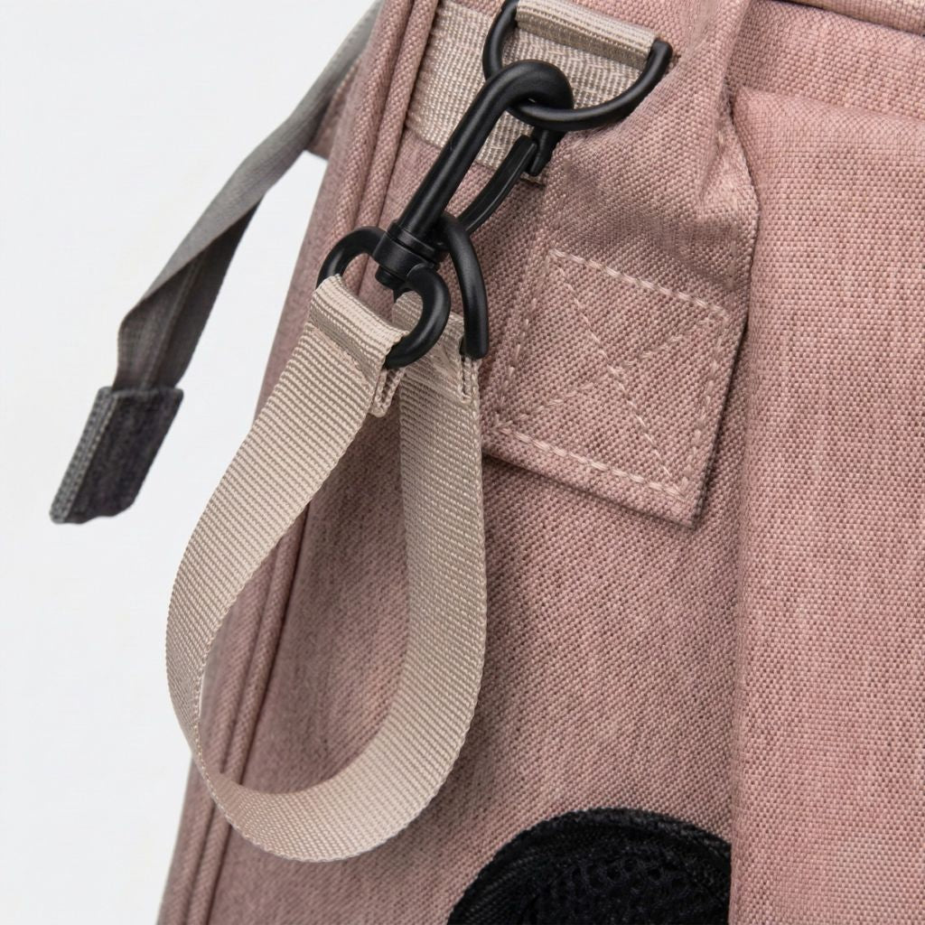 Gros plan du mousqueton noir mat et de la sangle beige sur le sac à langer rose poudré, détail robuste