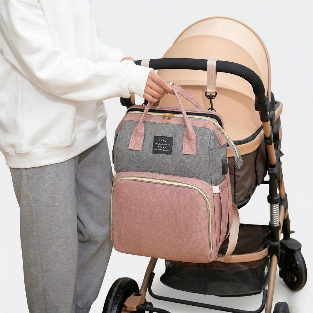 Lifestyle : parent fixant le sac à langer rose poudré et gris bicolore sur une poussette dorée