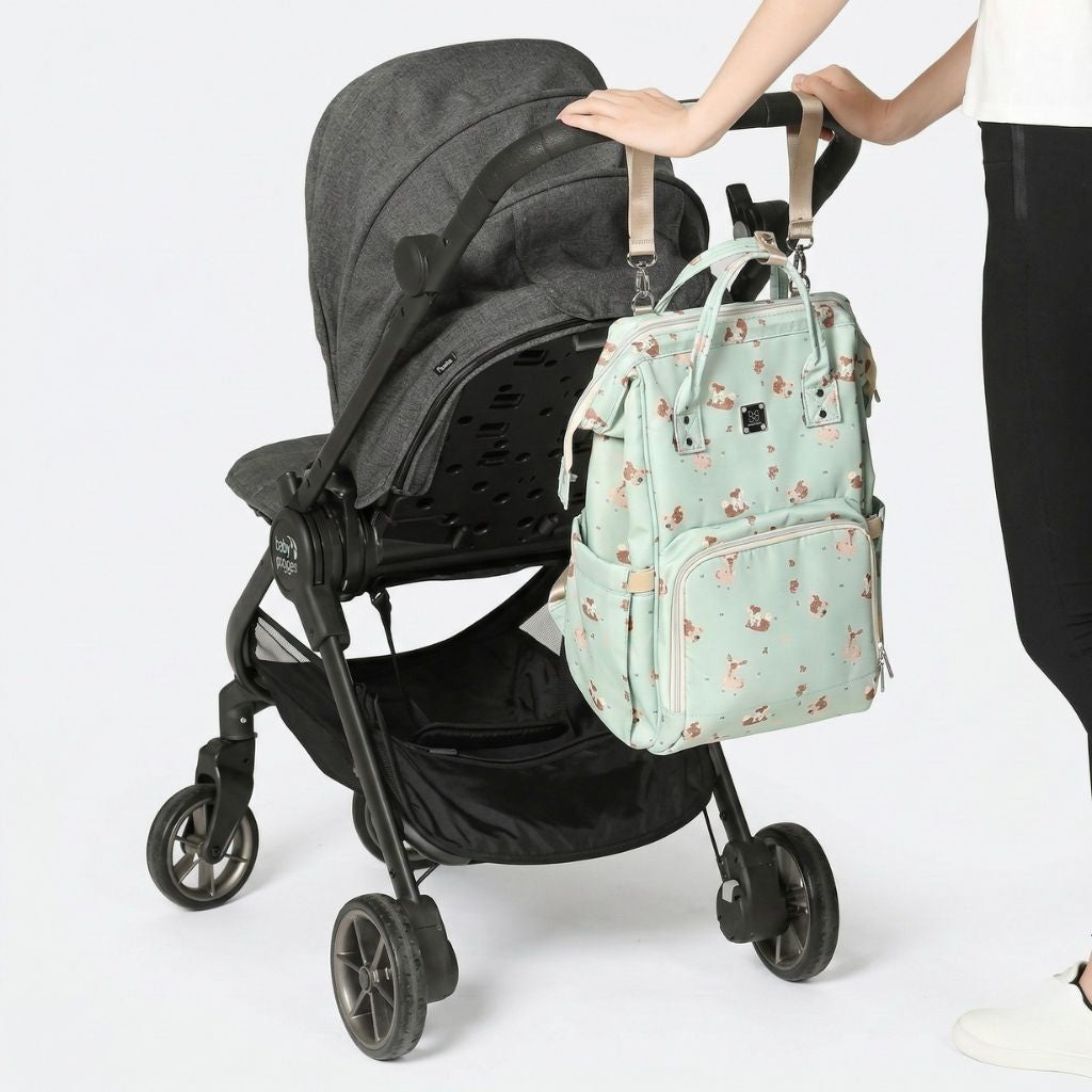 Sac à langer vert sauge avec motif animaux accroché à une poussette noire grâce aux passants intégrés