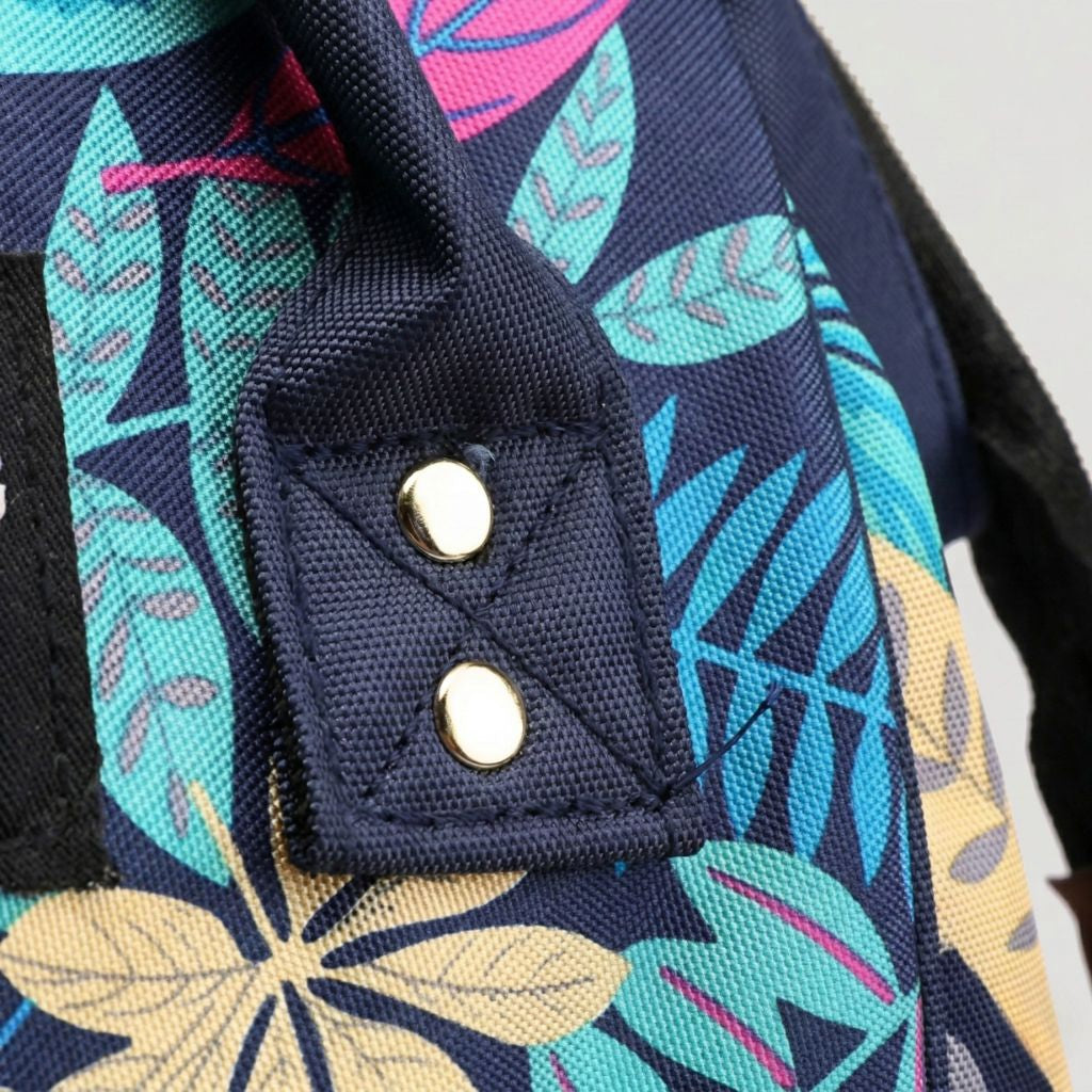 Gros plan sur les boutons dorés fixant les poignées du sac à langer sur le tissu bleu marine floral