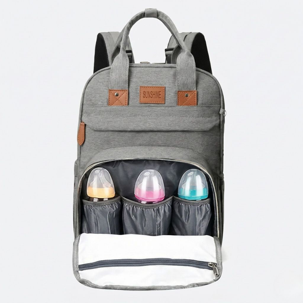 Sac à langer gris chiné compartiment isotherme chargé avec trois biberons colorés et tapis à langer blanc